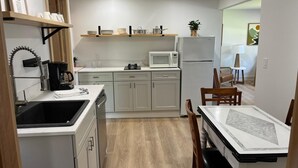 A compact kitchen with a sink, stove, microwave, and refrigerator. There is a dining table with chairs and a small plant on the counter. - Cottage #4 - Beautiful 3 Bedroom Lakefront Cottage - Fully Renovated in 2024! (Ashville)