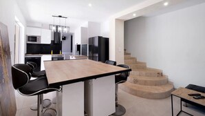 Une cuisine moderne avec un îlot central, des chaises noires et un escalier menant à un autre niveau.