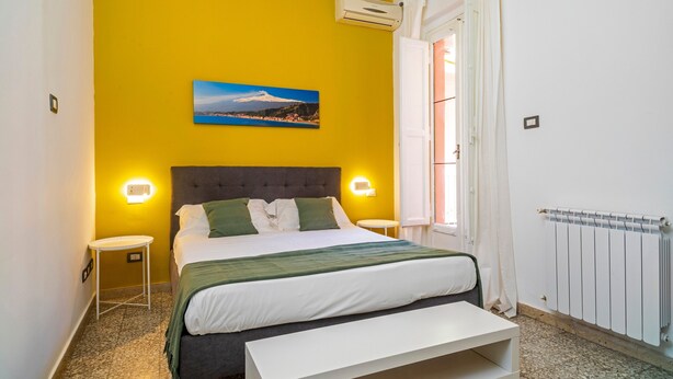 A bedroom with a bed, bedside tables, a bench, a painting, and a radiator.