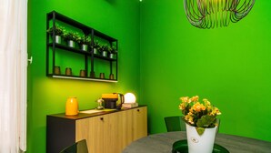 A room with a green wall, a wooden cabinet, a round table with a potted plant, and a black shelf with plants.