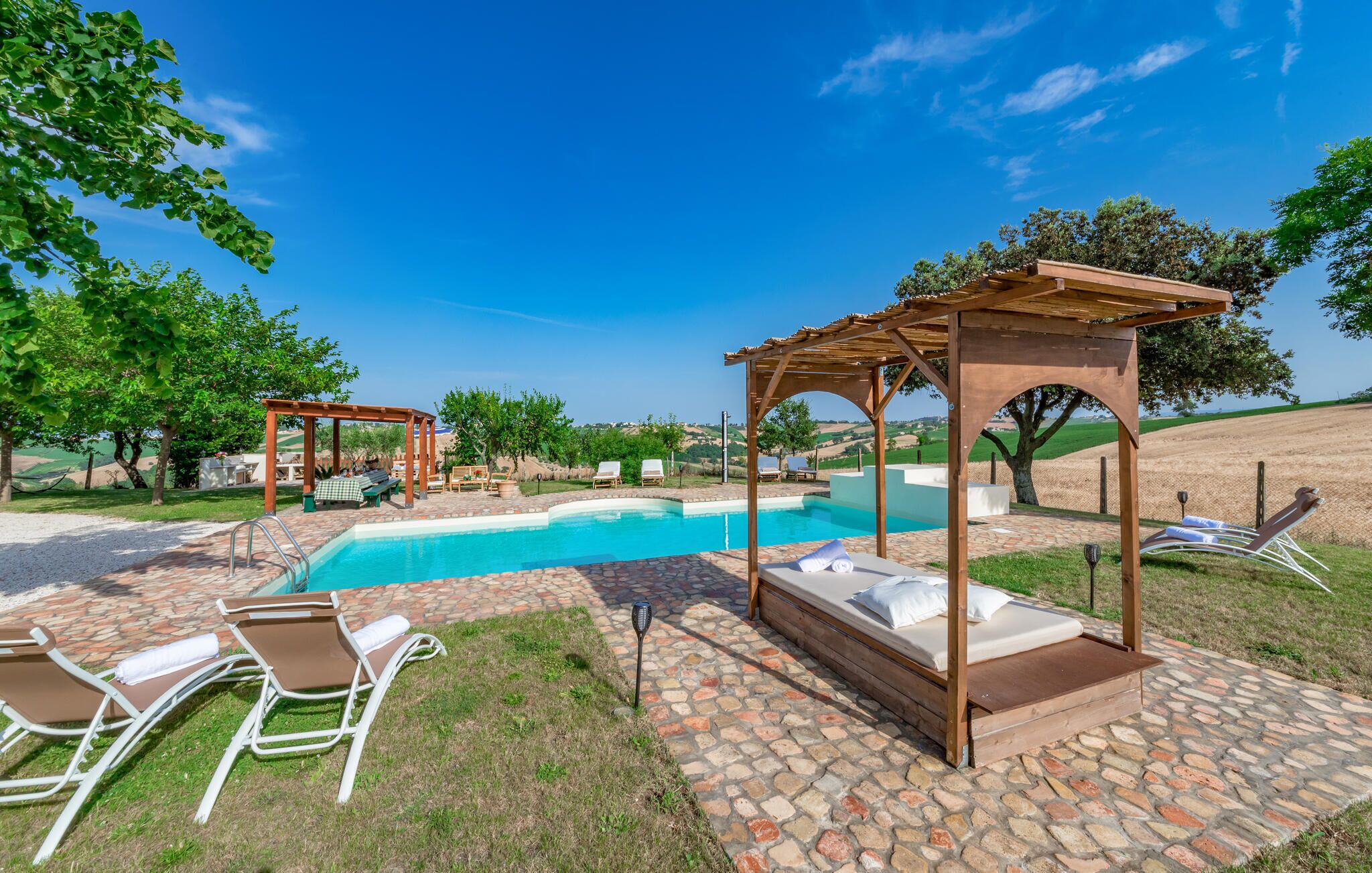 A poolside area with a pergola, lounge chairs, and a bed with a view of the landscape.