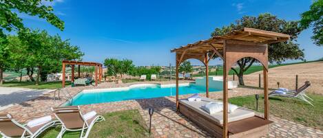 A poolside area with a pergola, lounge chairs, and a bed with a view of the landscape.