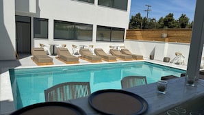 Un área de piscina exterior moderna con sillones de descanso y un bar.