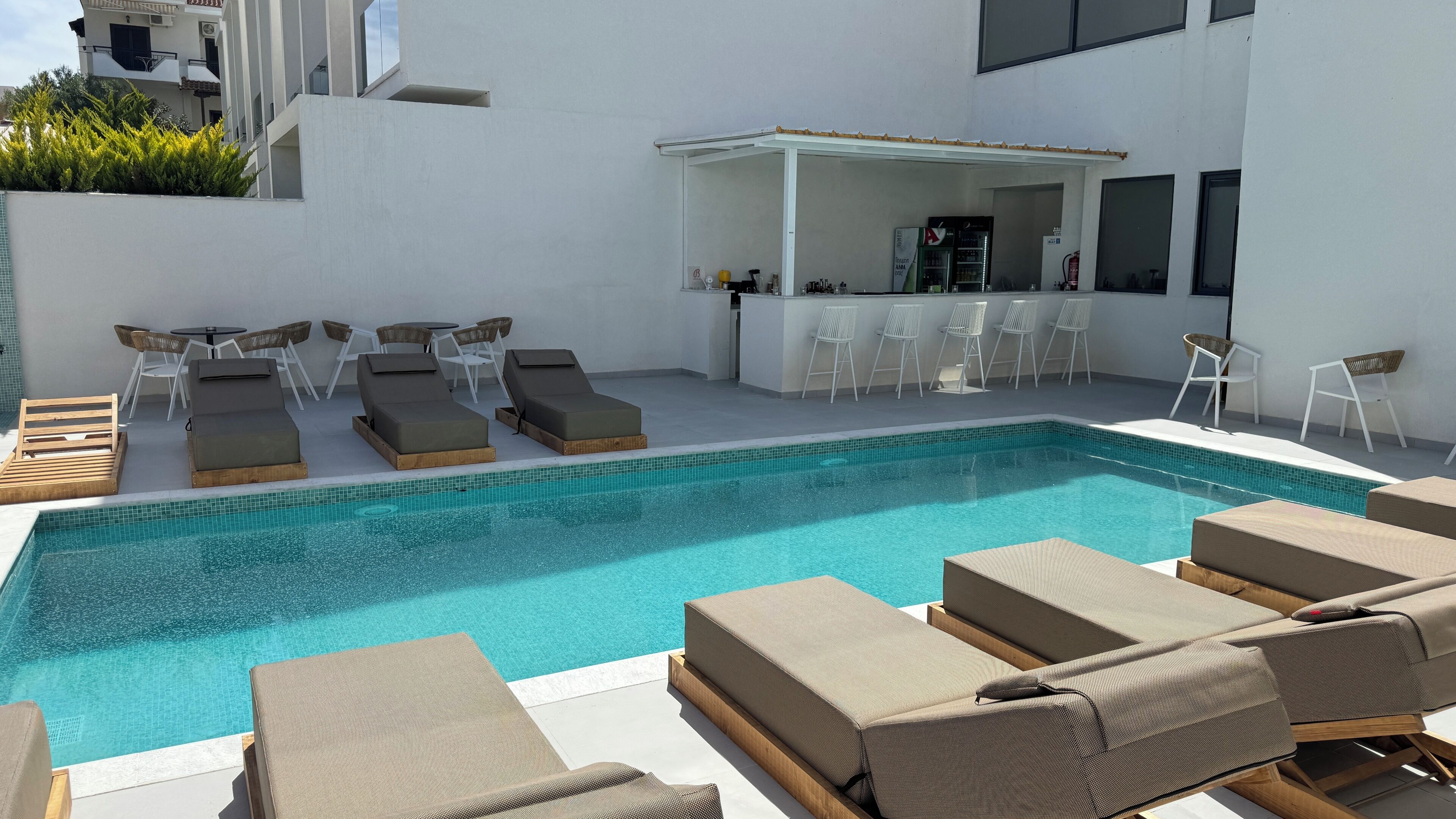 A modern outdoor pool area with lounge chairs and a bar.
