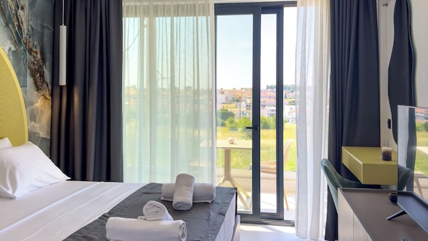Habitación de hotel con cama, escritorio, silla, televisor y un amplio ventanal con vista a la ciudad.