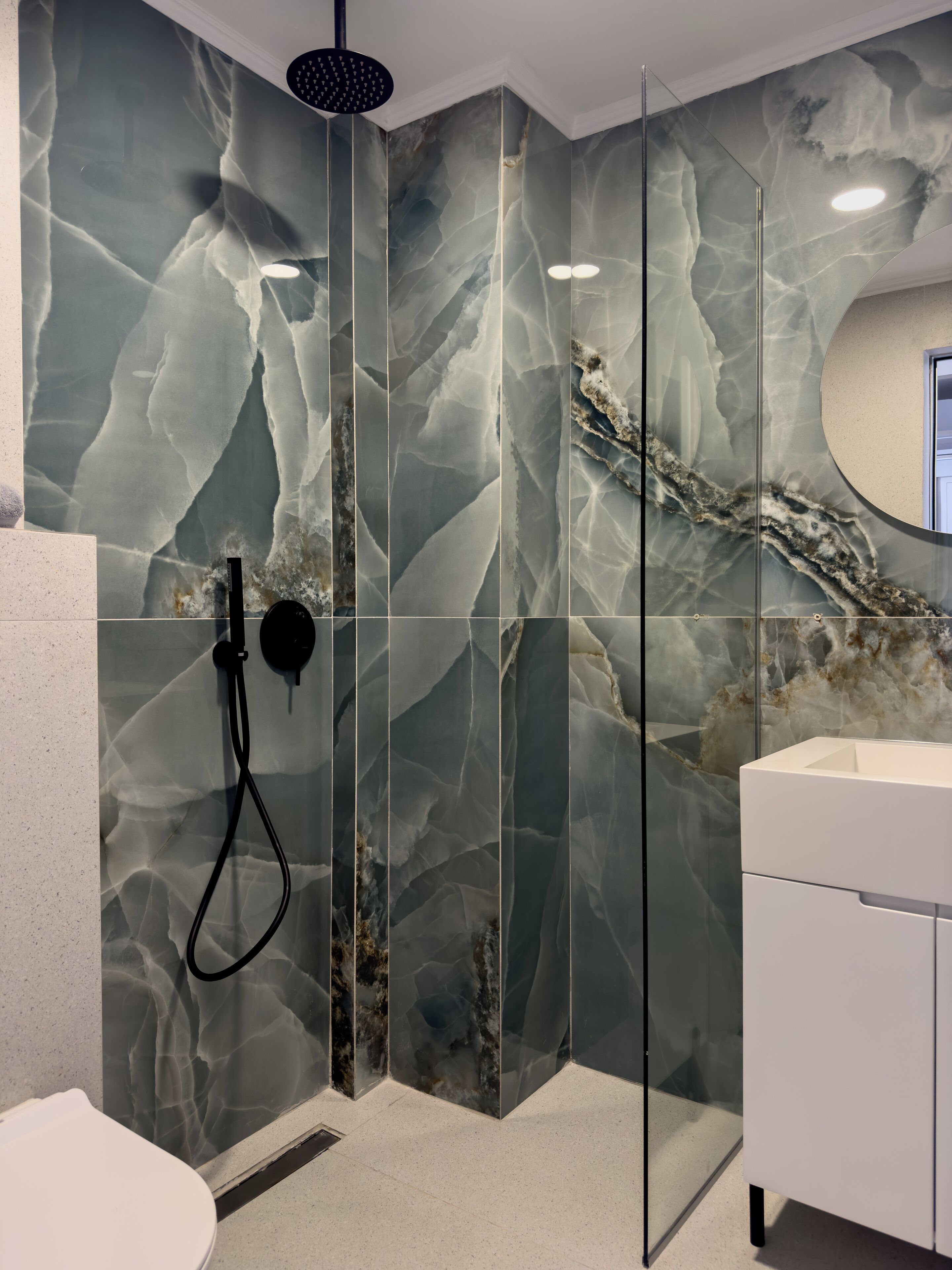 Une salle de bain moderne avec une douche à parois de verre, un lavabo blanc et des murs à motifs de marbre.