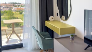 Una habitación de hotel moderna con un gran ventanal, una silla verde, una mesita de consola amarilla, un televisor de pantalla plana y un equipo de aire acondicionado.