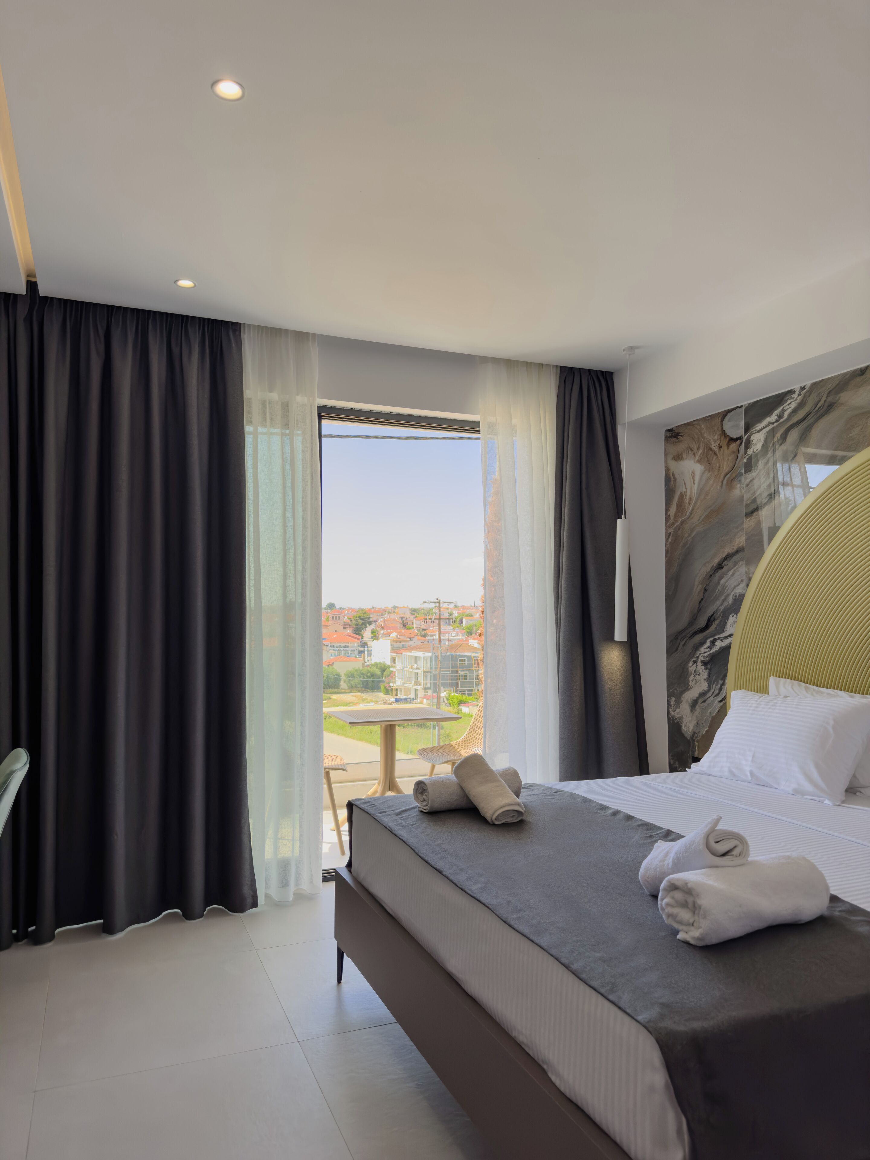 A hotel room with a bed, a chair, a table, and a view of the city.