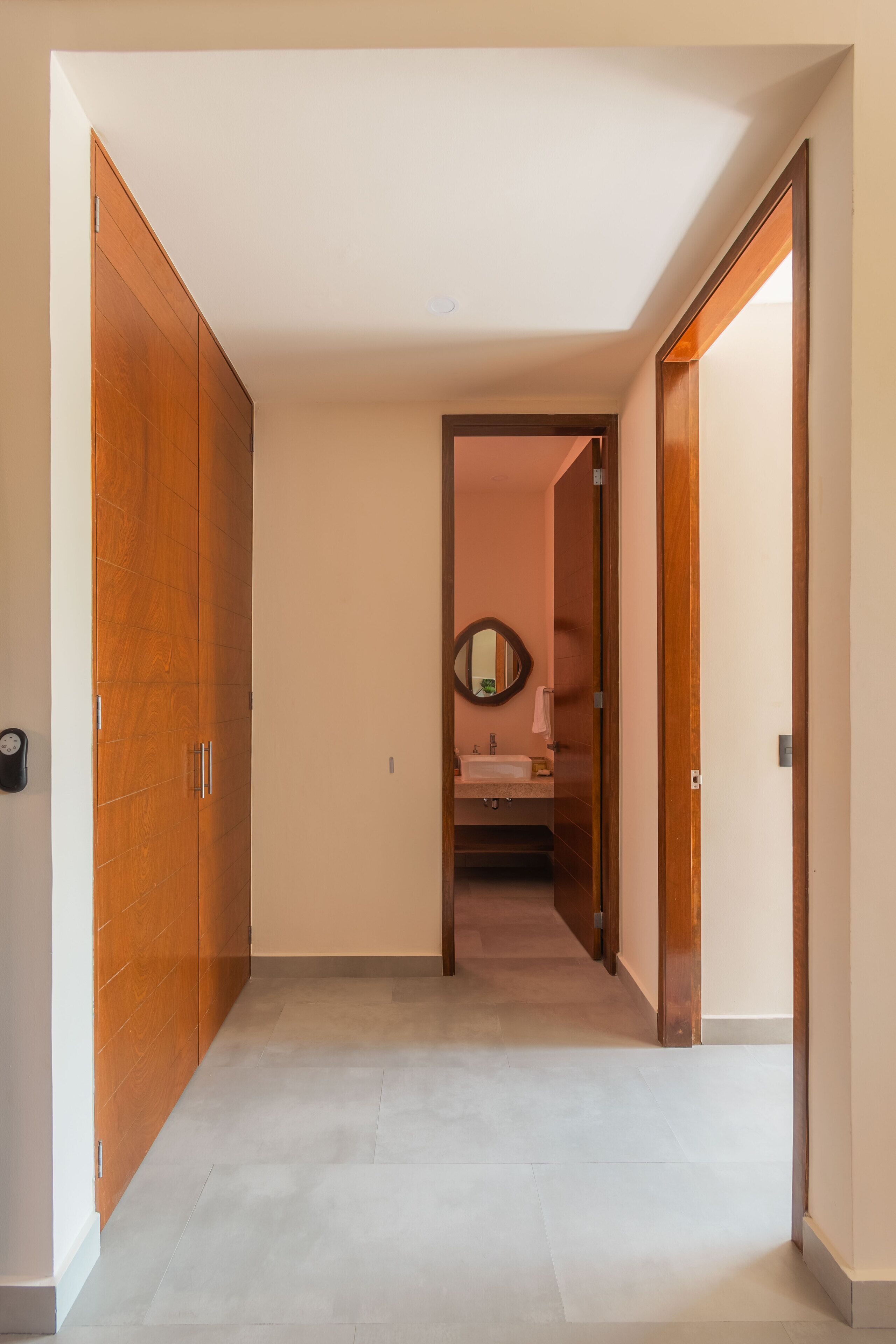 A hallway with a wooden wardrobe, a bathroom with a sink and mirror, and a tiled floor.
