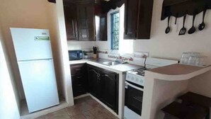 Una cocina compacta con armarios de madera oscura, un refrigerador blanco, una estufa y un lavamanos.