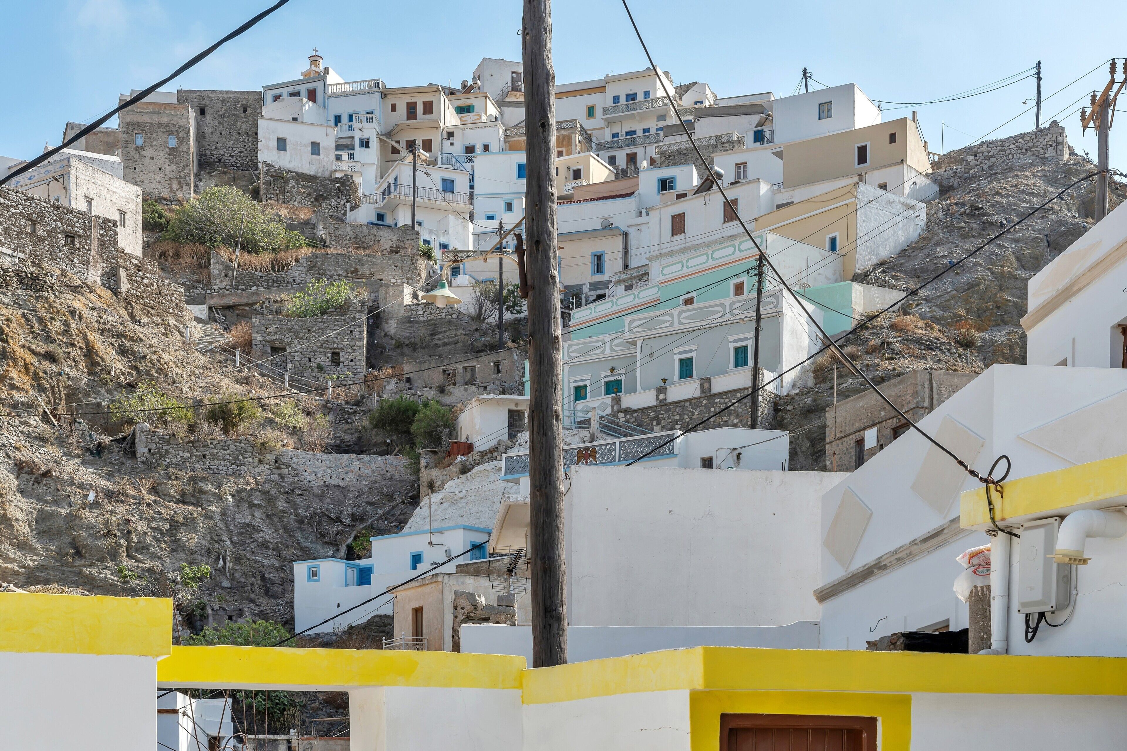 A hillside village with white buildings, a stone wall, and a yellow building in the foreground.