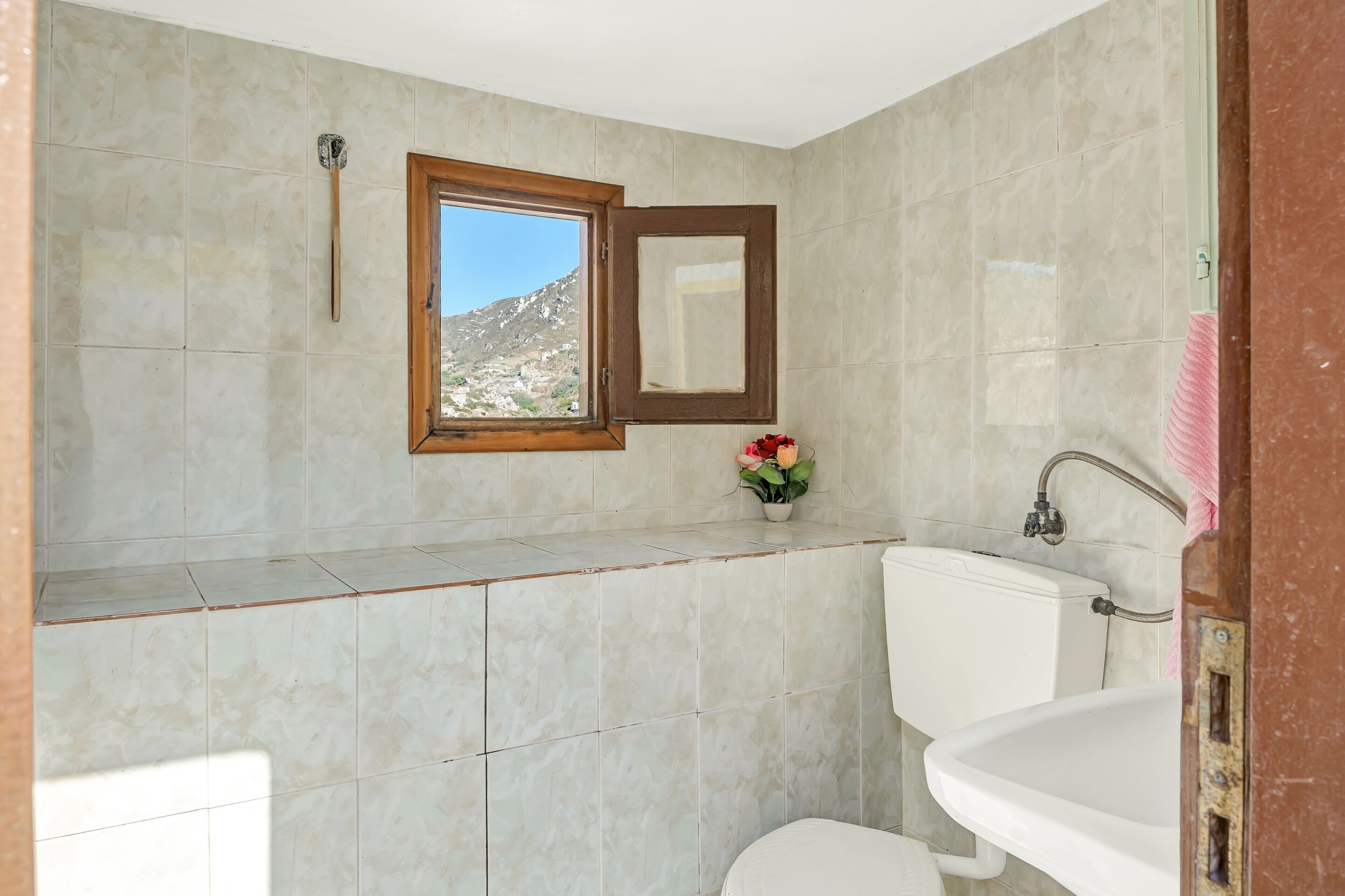 A bathroom with a toilet, sink, and window with a view of a mountain.