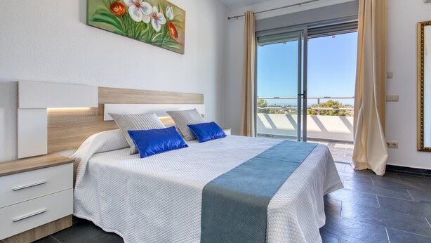 Un dormitorio con una cama, una mesita de noche, un cajón, un cuadro y vistas por una puerta corredera.