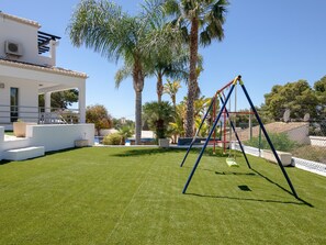 A well-maintained lawn with a swing set, palm trees, and a modern building with a balcony. - Villa 'Fustera' with Private Pool, Wi-Fi and Air Conditioning (Benissa)