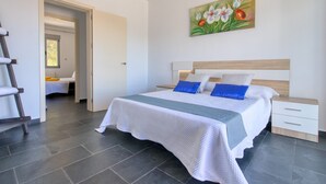 Un dormitorio con cama, mesita de noche, un cuadro y una puerta que da a otra habitación.