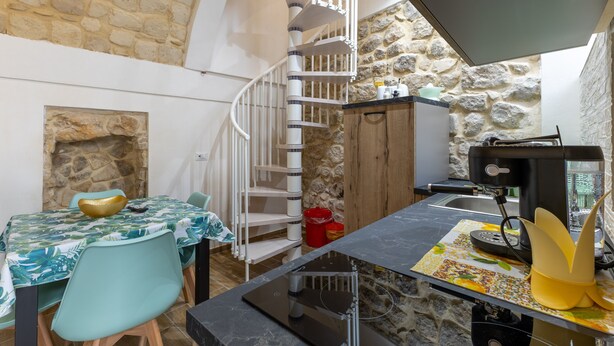 Eine Küche mit Steinwand, einer Wendeltreppe, einem Esstisch mit Stühlen und einer Kaffeemaschine.