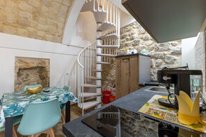 A kitchen with a stone wall, a spiral staircase, a dining table with chairs, and a coffee machine. - Apartment 'La Chicca Di Claudia' (Scicli)