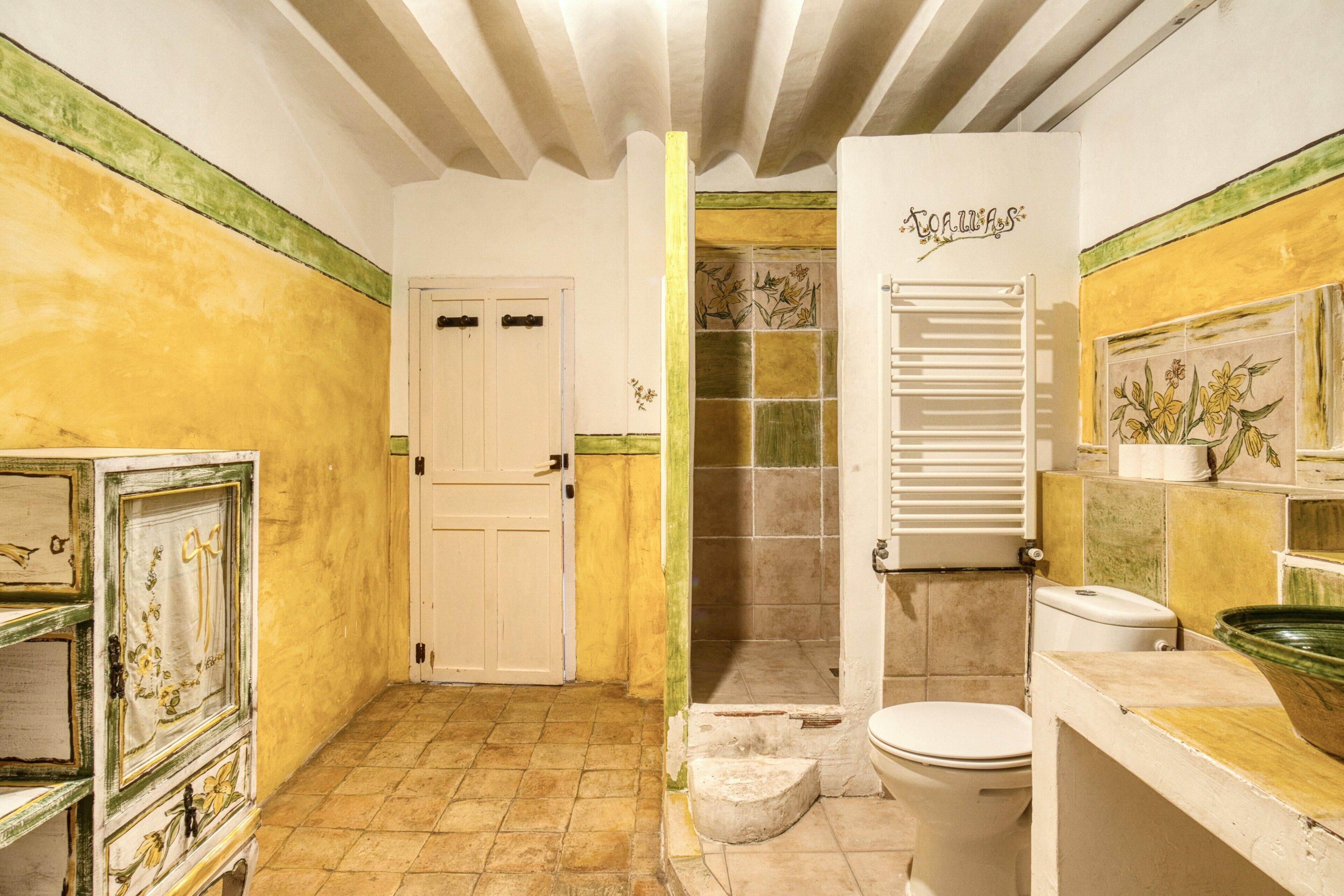 Une salle de bain comprenant des toilettes, un lavabo, une douche et une porte donnant sur une autre pièce.