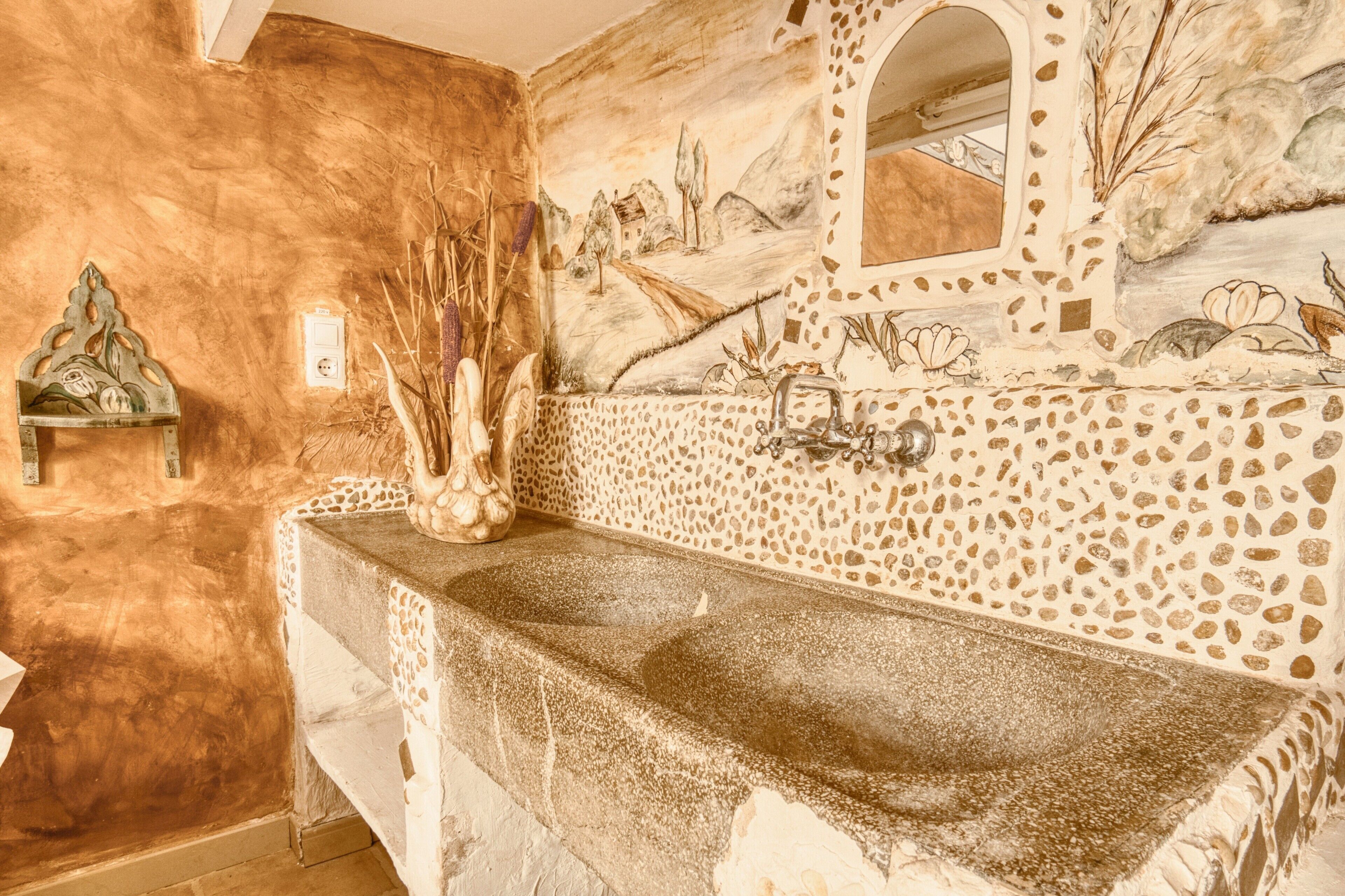 Une salle de bain avec un lavabo en pierre, un miroir et une fresque murale.