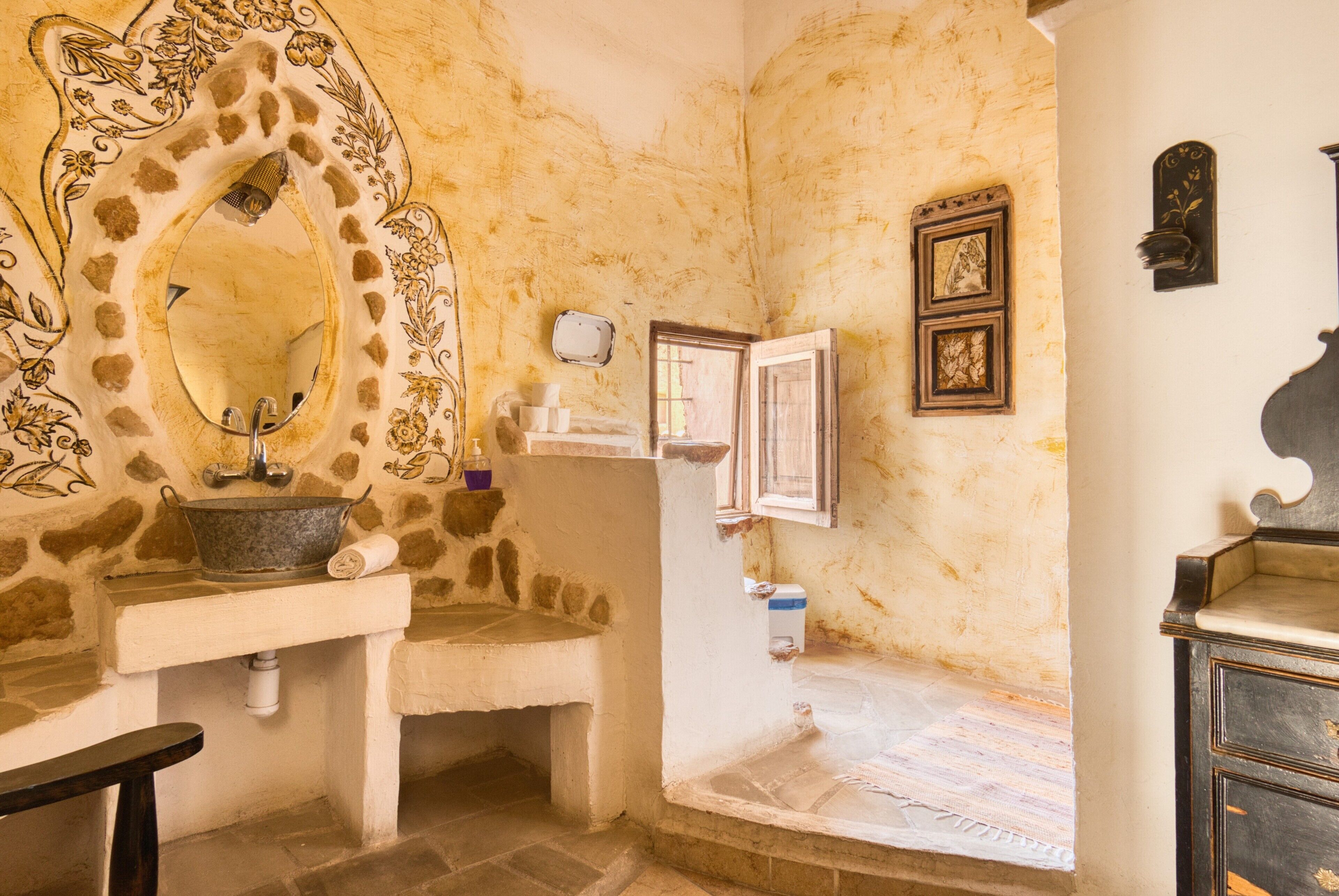A bathroom with a stone sink, a mirror with an ornate frame, a small window, and a wall-mounted shelf.