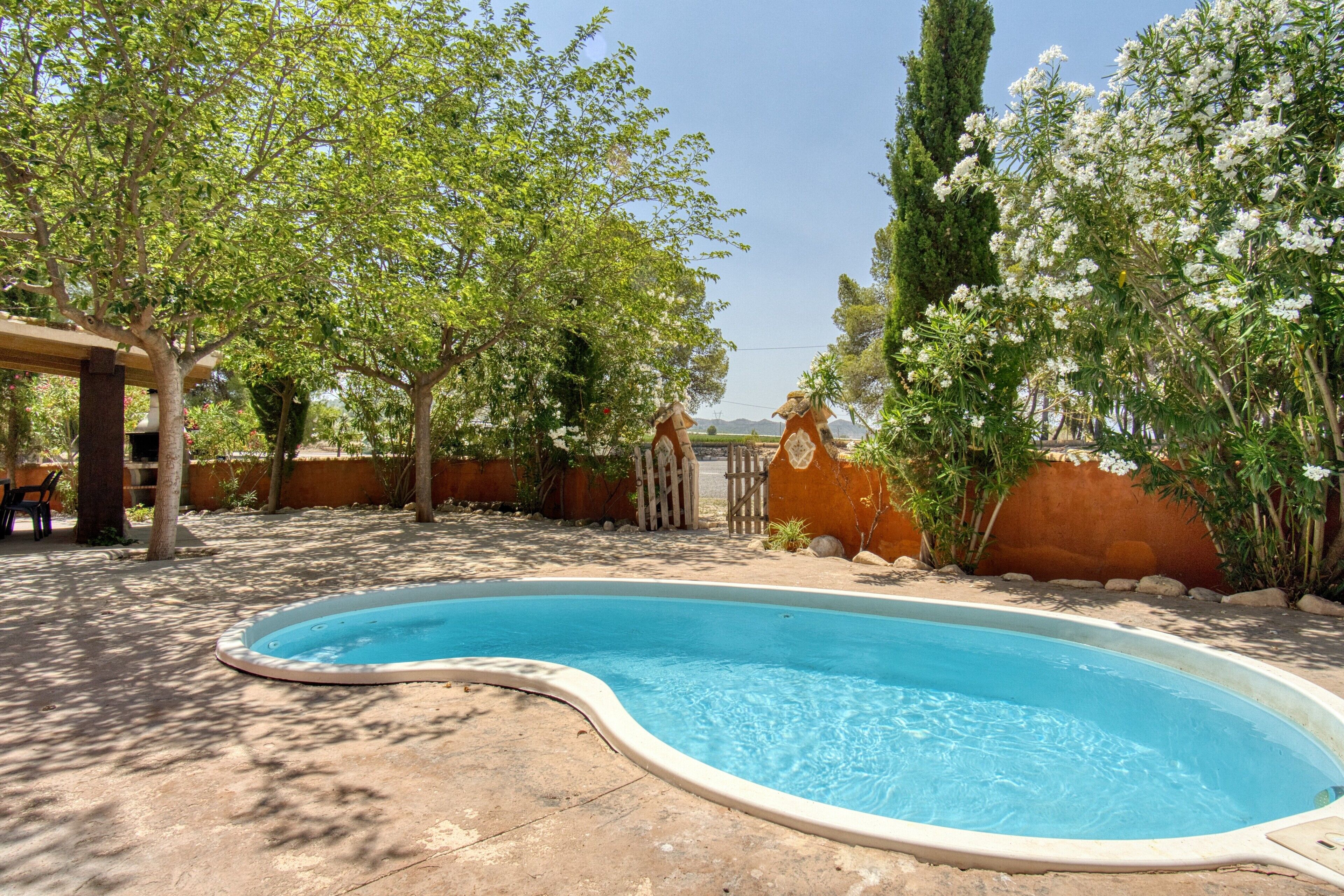 Una piscina de borde curvo, rodeada de árboles y una valla de madera.