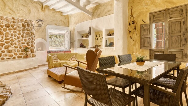 A cozy room with a stone wall, a sofa, a dining table with chairs, and a window with a view.