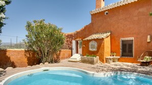 A swimming pool with a stone edge, a small white door, and a window with a metal grille.