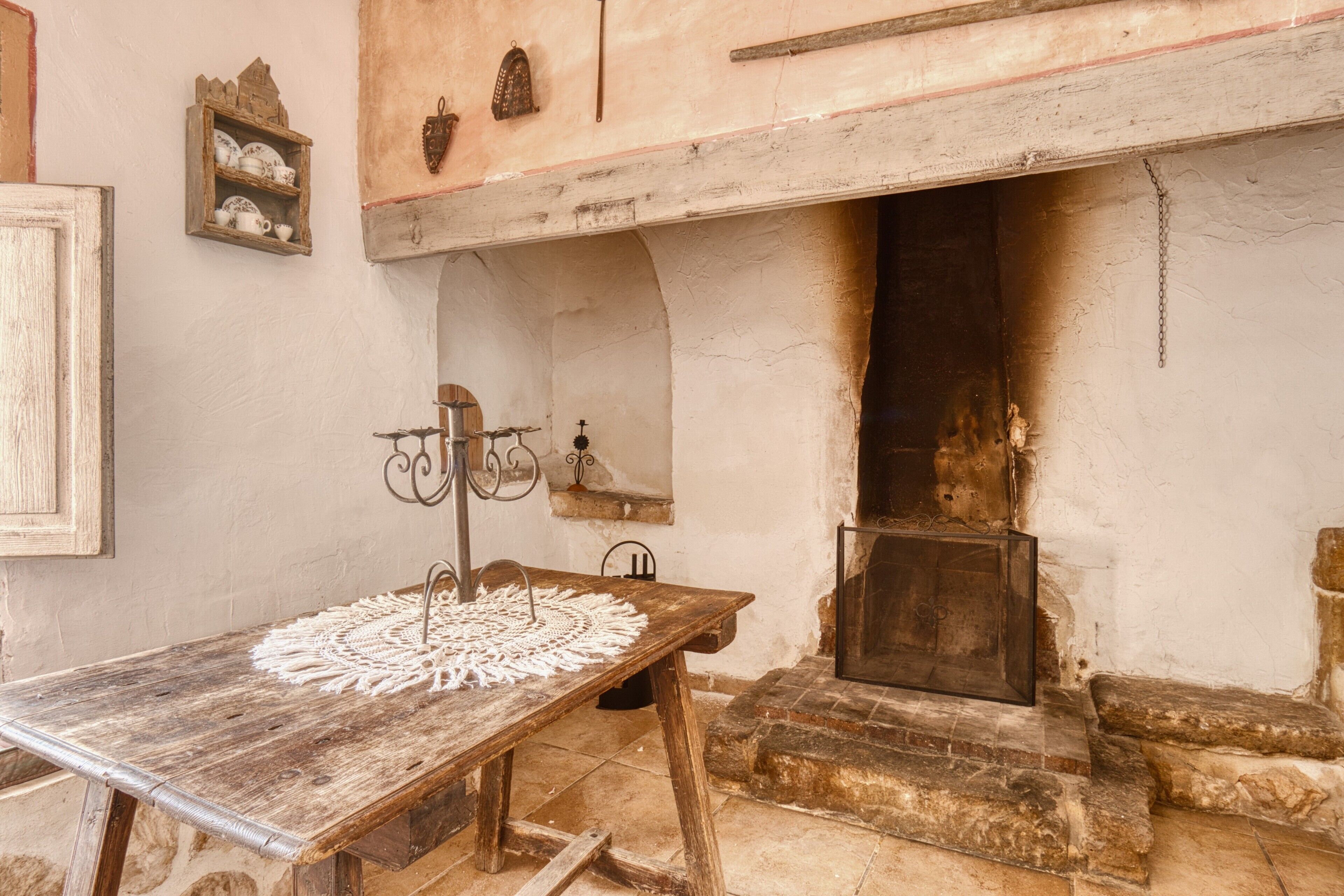 Una habitación rústica con una mesa de madera, una chimenea y una estantería con adornos.
