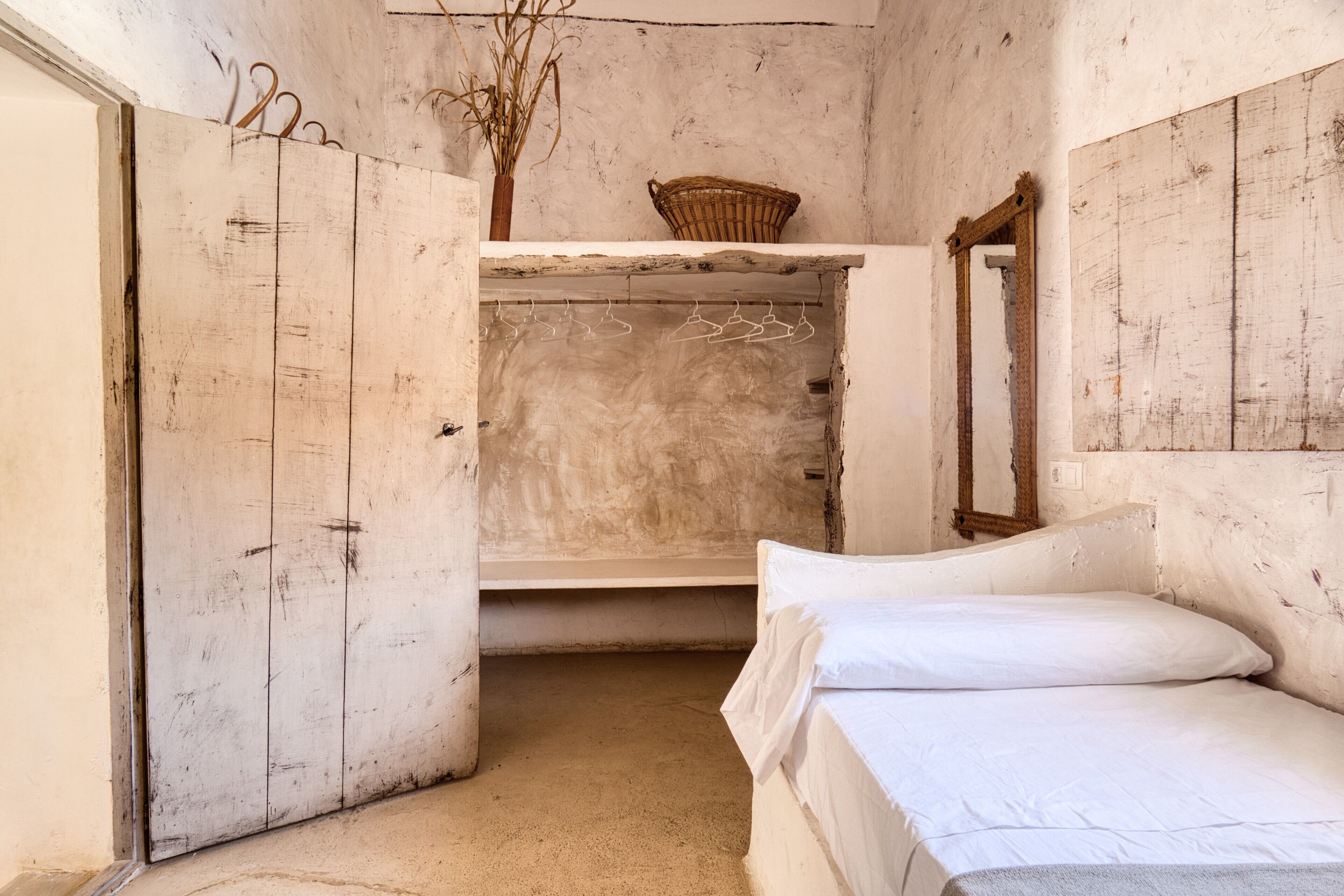 A room with a bed, a hanging clothes rack, a basket, and a mirror.