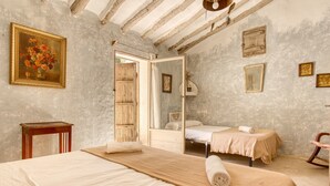 A bedroom with a large bed, a smaller bed, a wooden chair, a wooden table, and a painting on the wall.