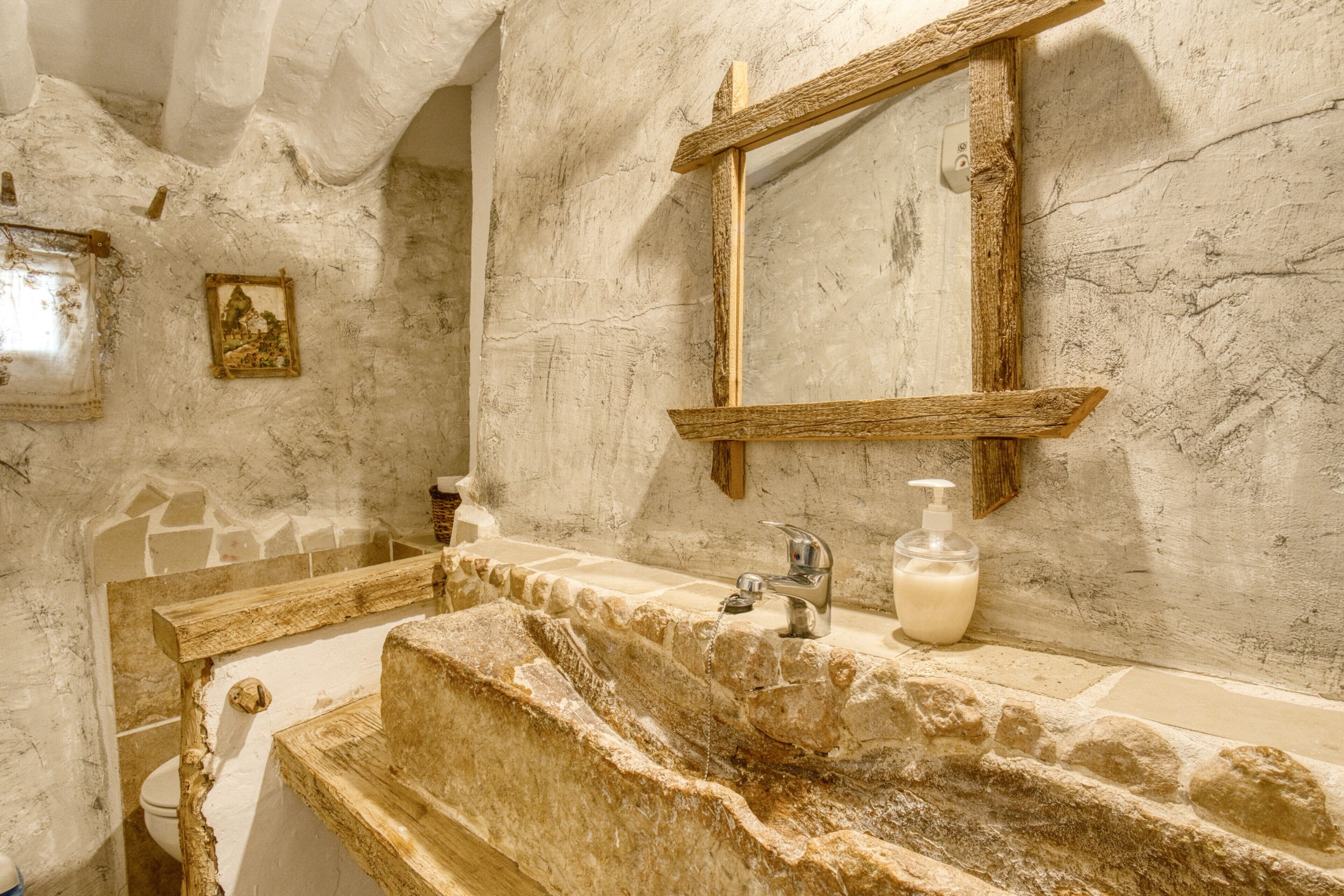 Un baño con lavamanos de piedra, un espejo y un inodoro.