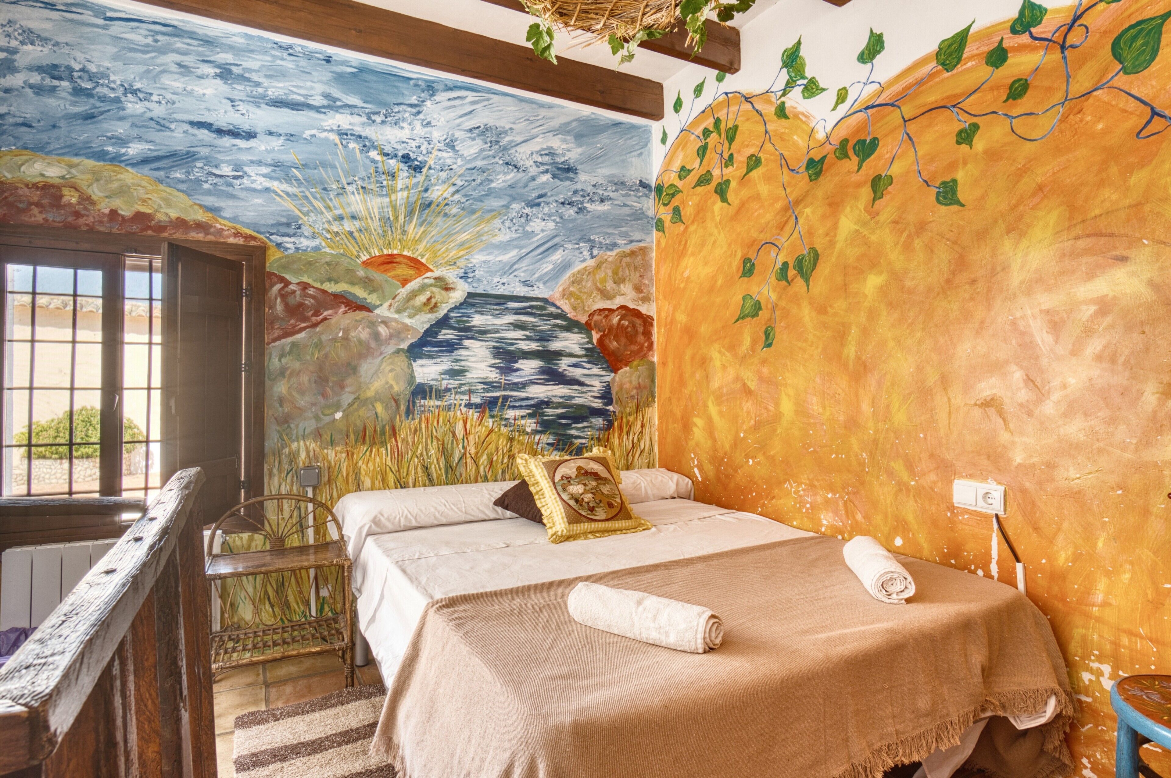 A room with two beds, a mural on the wall, and a window with a view.