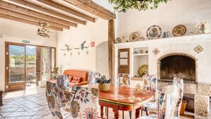 A dining area with a table and chairs, a fireplace, and a view through a door. - Country House 'Madara' with Mountain Views, Private Pool and Wi-Fi (Monòver)