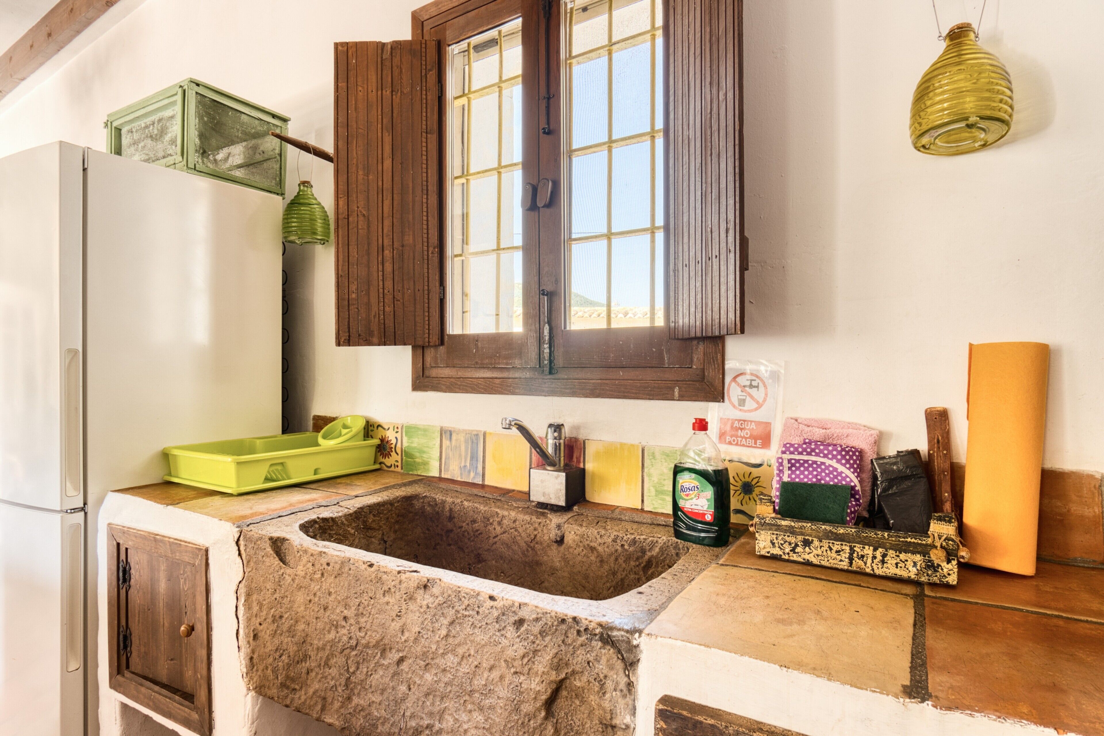 A kitchen with a stone sink, wooden cabinets, a window with shutters, and a hanging light fixture.