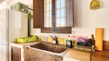 A kitchen with a stone sink, wooden cabinets, a window with shutters, and a hanging light fixture.