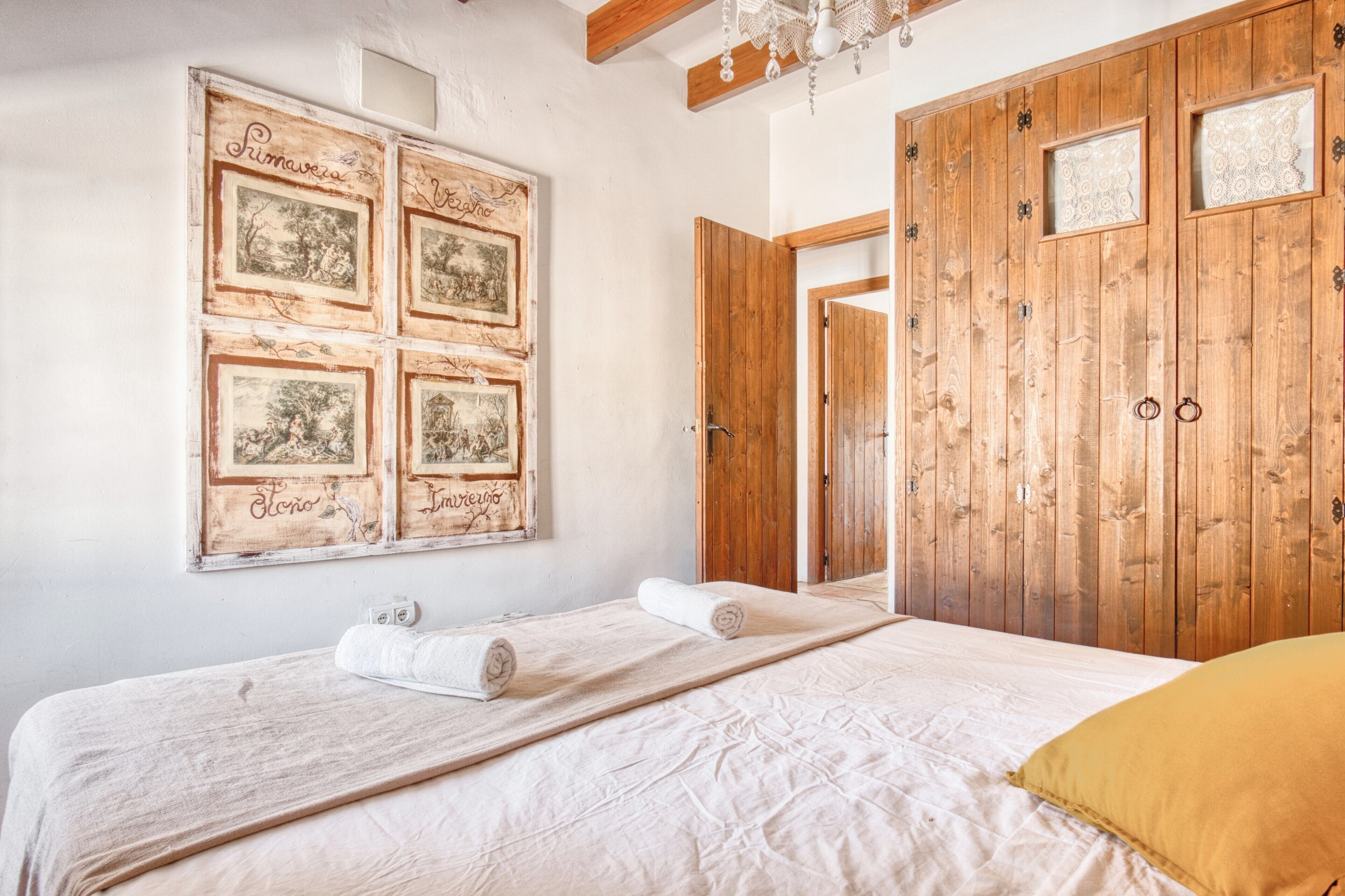 A bedroom with a bed, a wooden wardrobe, and a wall with framed pictures.