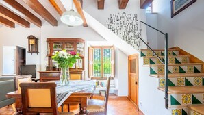 A dining area with a wooden table, chairs, a vase of flowers, and a view of the outside through a window. - Holiday Home 'Ca'n Repic' with Mountain View, Private Terrace and Wi-Fi (Illes Balears)