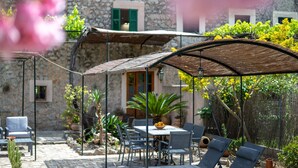 A stone building with a patio area featuring a table and chairs, surrounded by potted plants and a pergola. - Holiday Home 'Ca'n Repic' with Mountain View, Private Terrace and Wi-Fi (Illes Balears)