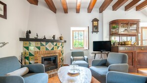 A living room with a fireplace, blue armchairs, a television, and a wooden cabinet. - Holiday Home 'Ca'n Repic' with Mountain View, Private Terrace and Wi-Fi (Illes Balears)