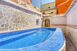 A swimming pool with mosaic tile flooring, a stone wall, and a building with a tiled roof in the background. - Country House 'Señores Y Tía Juana' with Mountain View, Private Pool and Wi-Fi (Monovar)