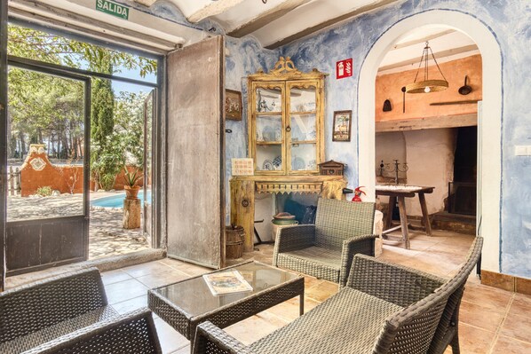A room with wicker furniture, a glass table, a cabinet with glass doors, and a view of the outside.