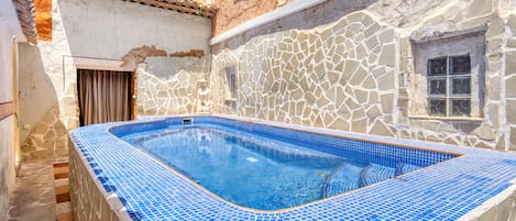 A swimming pool with blue mosaic tiles, a stone wall, and a window.