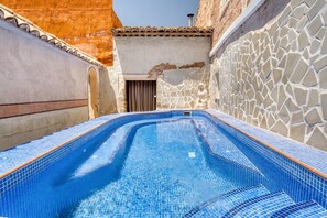 A swimming pool with mosaic tiles, a stone wall, and a tiled roof.