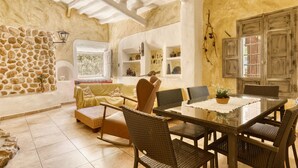 Une pièce chaleureuse avec un mur en pierre, un canapé, une table à manger avec des chaises et une fenêtre donnant sur un beau paysage.