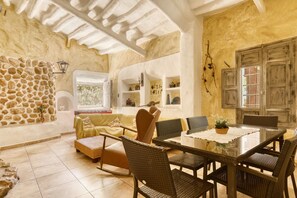 A cozy room with a stone wall, a sofa, a dining table with chairs, and a window with a view. - Country House 'Señores Y Tía Juana' with Mountain View, Private Pool and Wi-Fi (Monovar)