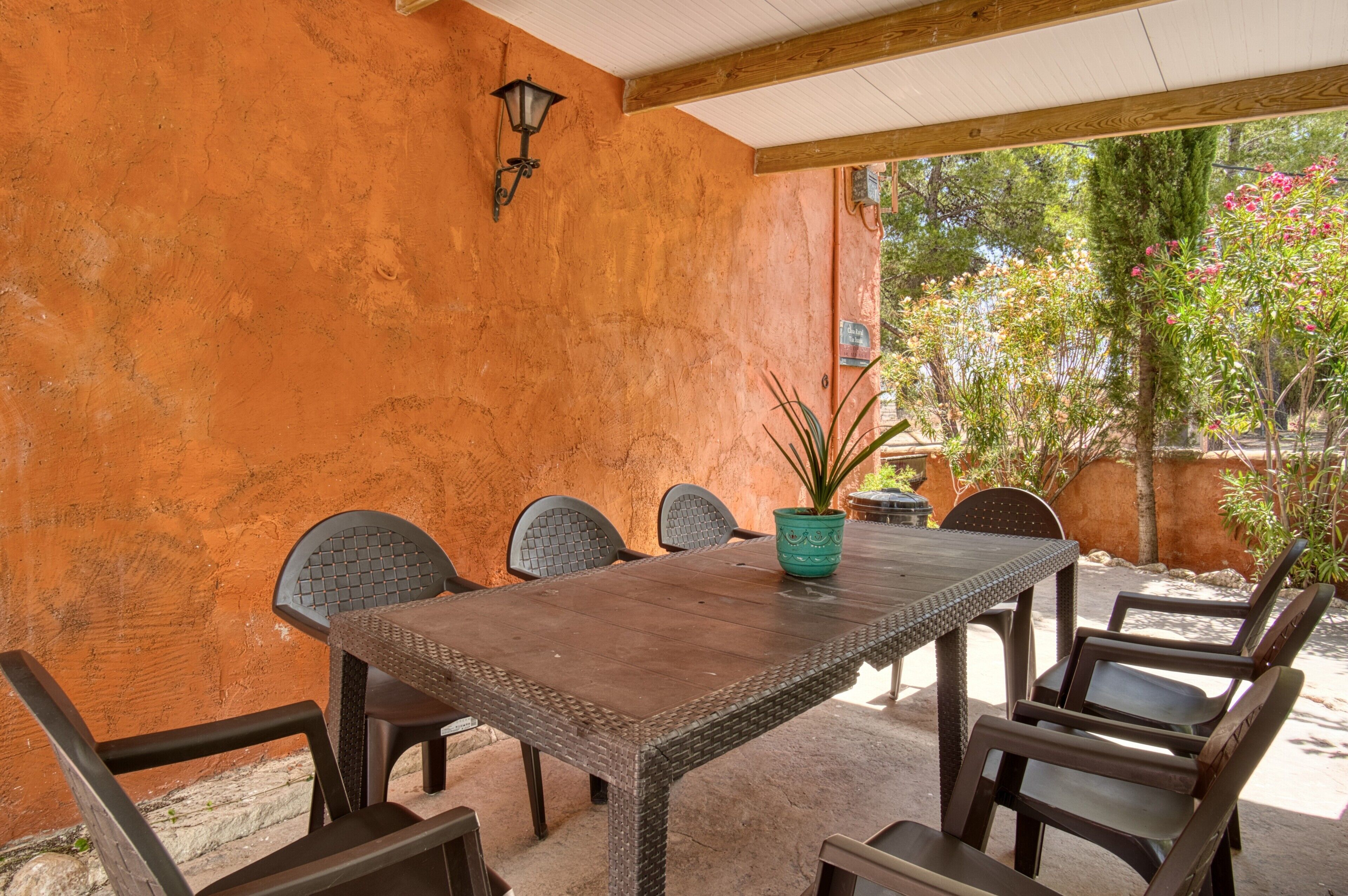 Un patio al aire libre con una mesa y sillas de madera, una planta en maceta y una lámpara fijada a la pared.