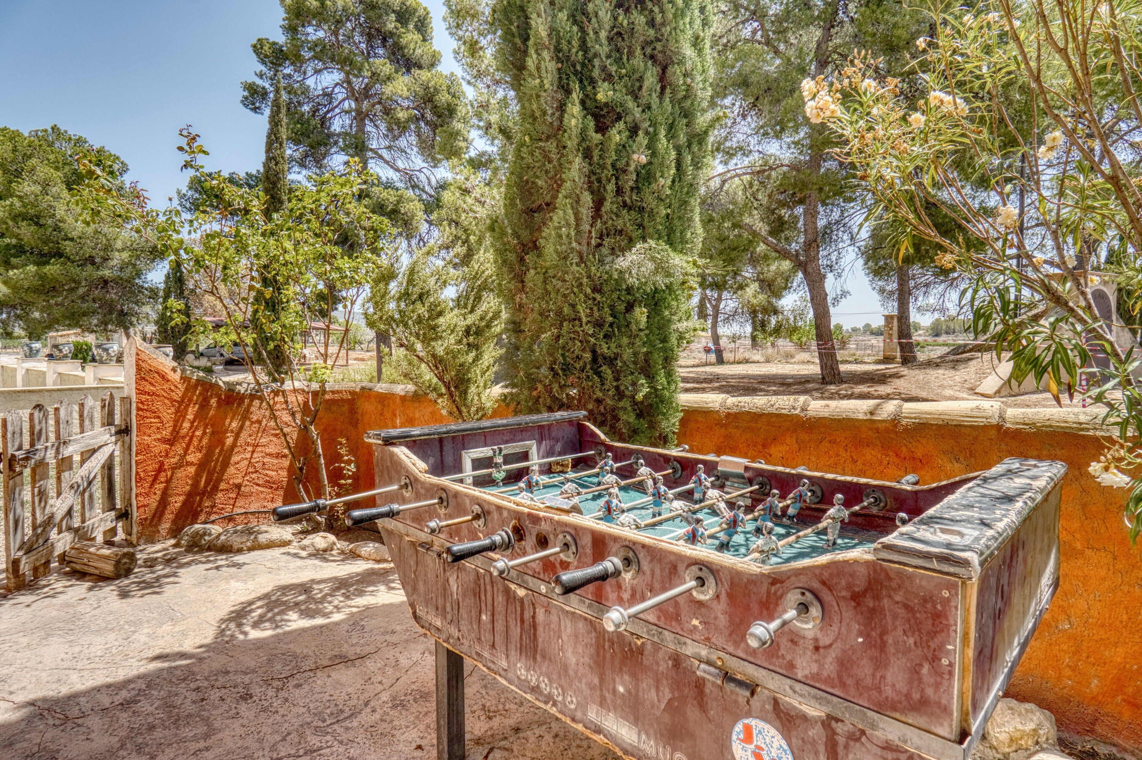 Una mesa de fútbol de mesa en un entorno exterior con árboles y una valla al fondo.