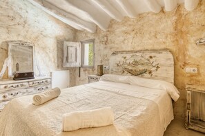 Une chambre à coucher avec un grand lit, une commode à motifs floraux, un miroir et un mur orné d’un tableau floral.