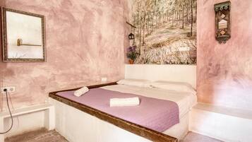 Een slaapkamer met een bed, een spiegel, een schilderij en een klein raam.