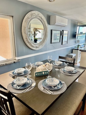 Uma mesa de jantar posta com pratos azuis e brancos, talheres e copos de vinho, com uma placa no centro que diz 'WELCOME'.